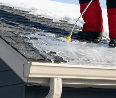 Ice dam removal technician using a steam wand to melt thick ice buildup on a residential roof in Boise, ID