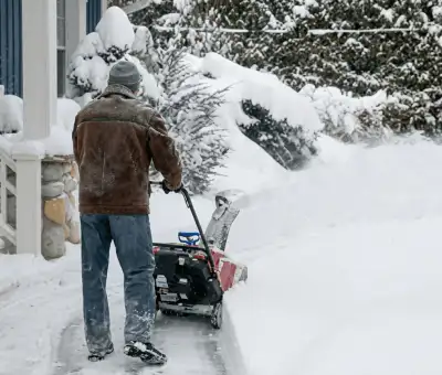 Residential snow removal technician using a snow blower to clear a home driveway and walkway in Boise, ID