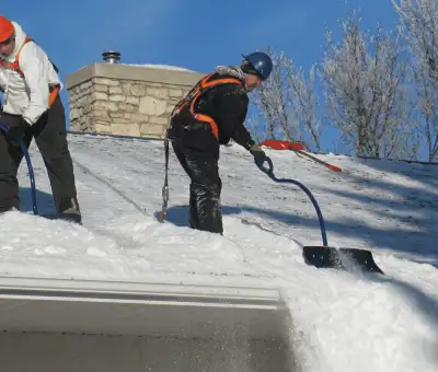 Professional technicians performing roof snow removal with safety harnesses and shovels in Boise, ID